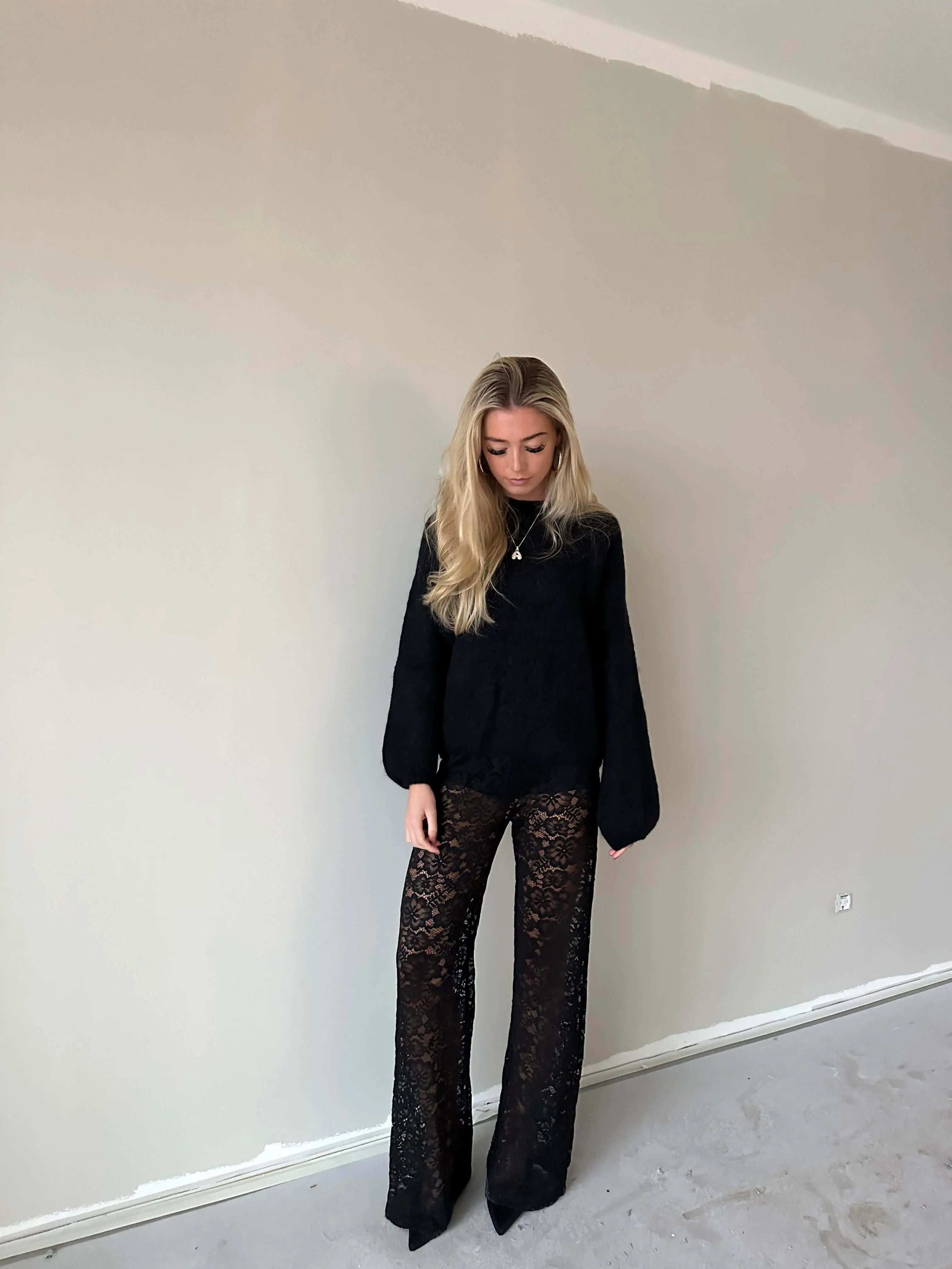 Woman wearing Valentina™ Luxe Kanten Broek with black lace detailing and a comfortable fit, standing against a light-colored wall.