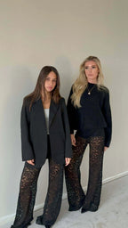 Two women wearing Valentina™ Luxe Kanten Broek with lace details and black tops, showcasing elegant and stylish outfits.