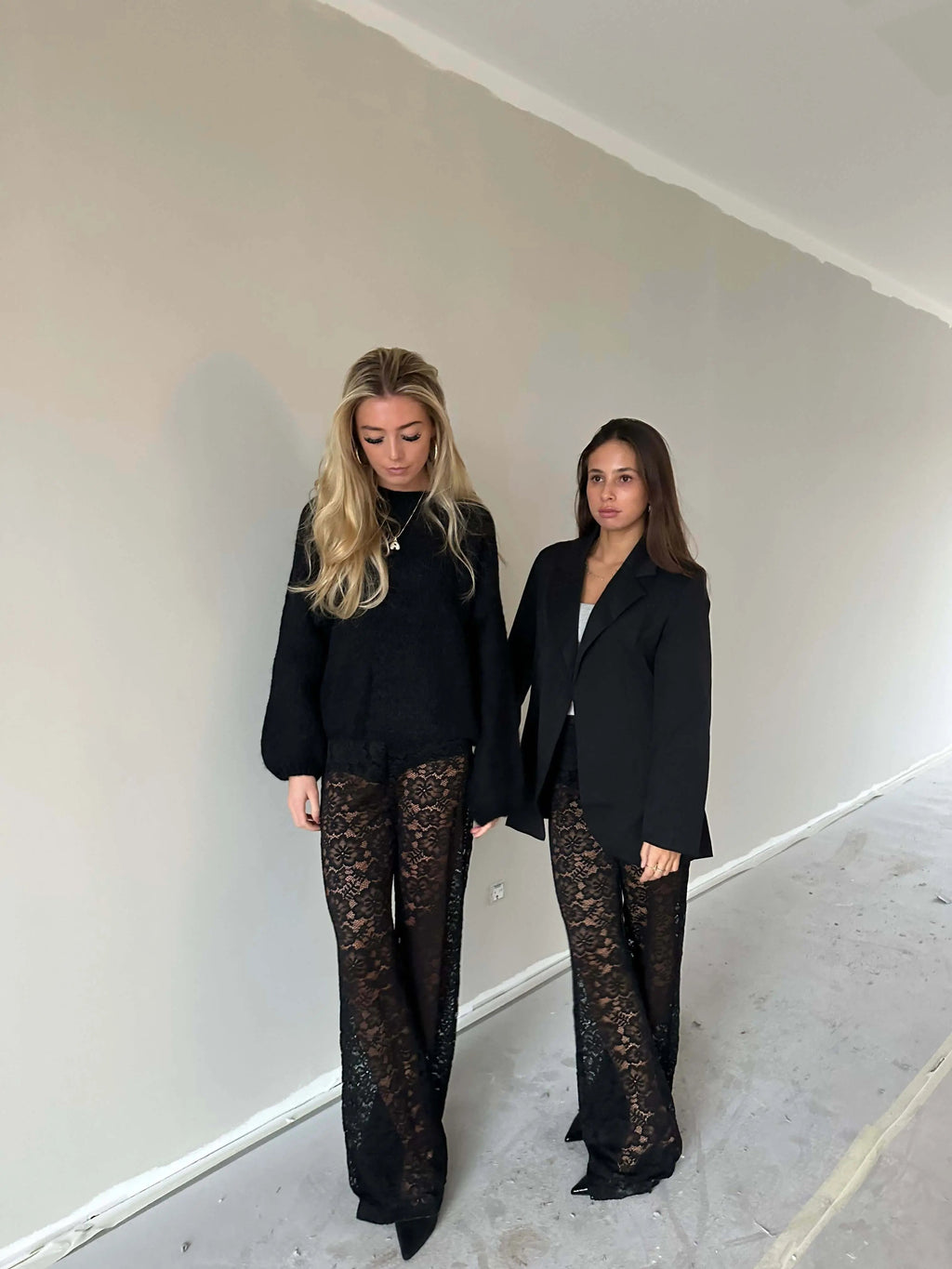 Twee vrouwen dragen de Valentina Luxe Kanten Broek, gecombineerd met stijlvolle zwarte tops, tonen elegantie en comfort.