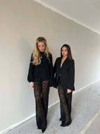 Twee vrouwen dragen de Valentina Luxe Kanten Broek, gecombineerd met stijlvolle zwarte tops, tonen elegantie en comfort.