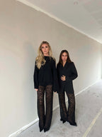 Two women wearing black tops and Valentina™ Luxe Kanten Broek with lace details in a neutral-toned room.