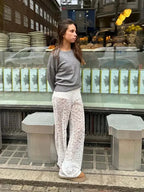 Woman wearing Valentina™ Luxe Kanten Broek with delicate lace details, pairing it with a grey sweater, standing in an urban setting.